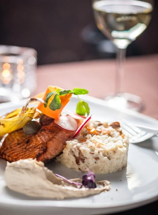 Grilled salmon with risotto, garnished with vegetables and served with a glass of white wine.