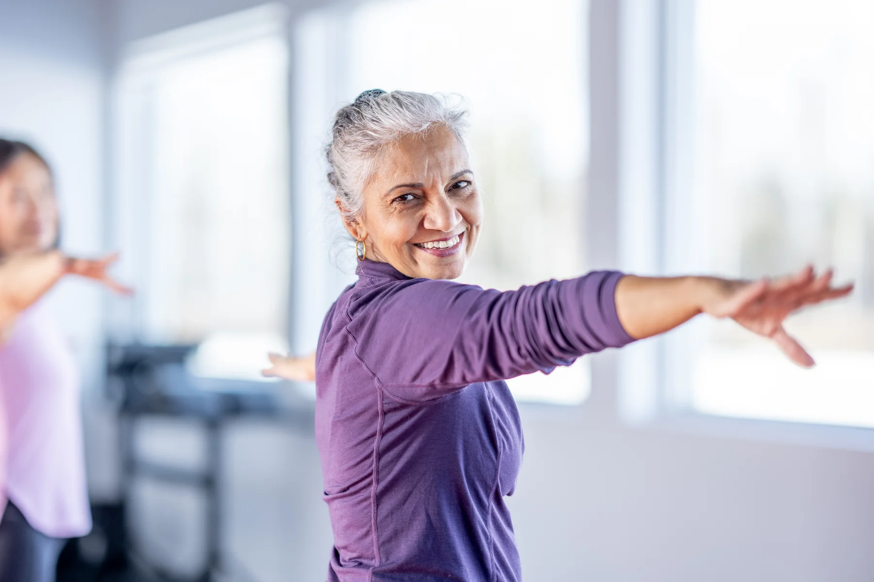 Smiling Senior Woman In Purple Activewear Demonstrates Balance And Exercise In Class