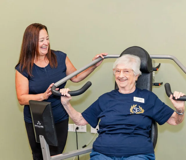 Fitness Supervisor Gina O'Leary helping a resident on strength training equipment at Oak Trace in Downers Grove, Illinois
