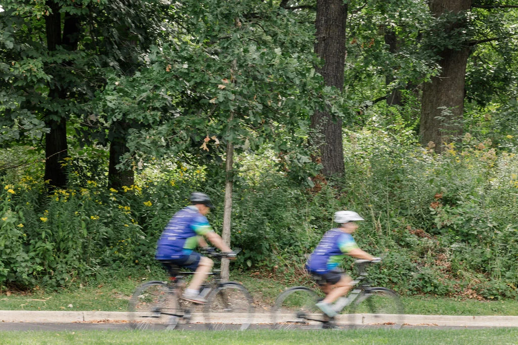 Chris Laperuto and Bill Roznowski riding a tree-lined trail together