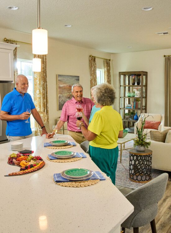 four seniors smile and gather for dinner in an apartment at Oak Trace Senior Living Community