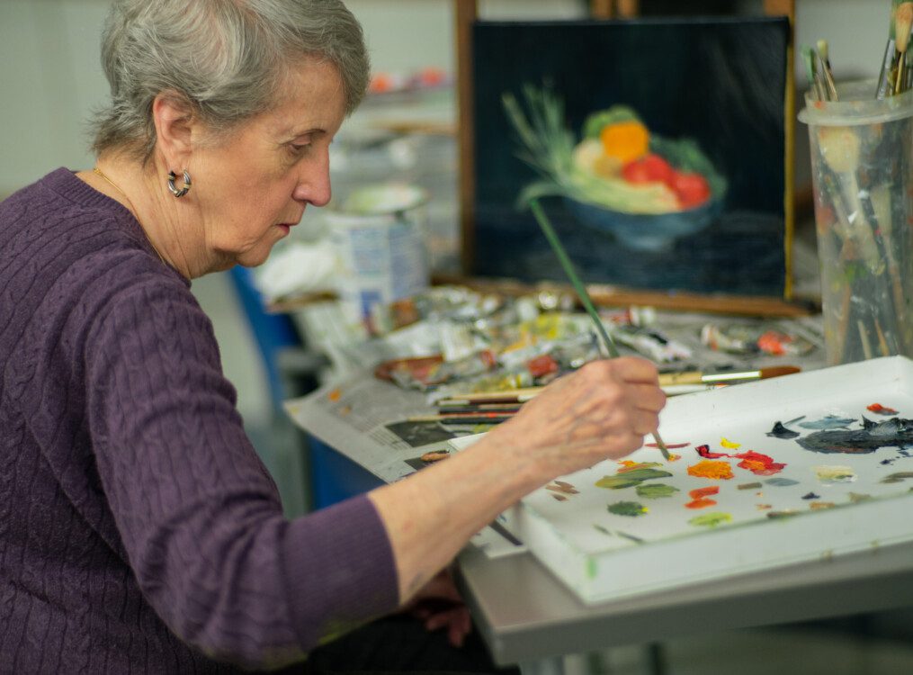 senior woman concentrates while painting during class