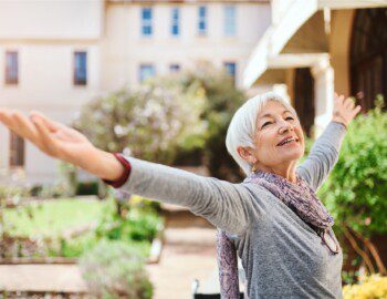 senior woman smiles up at the sky with her arms out, a look of freedom on her face