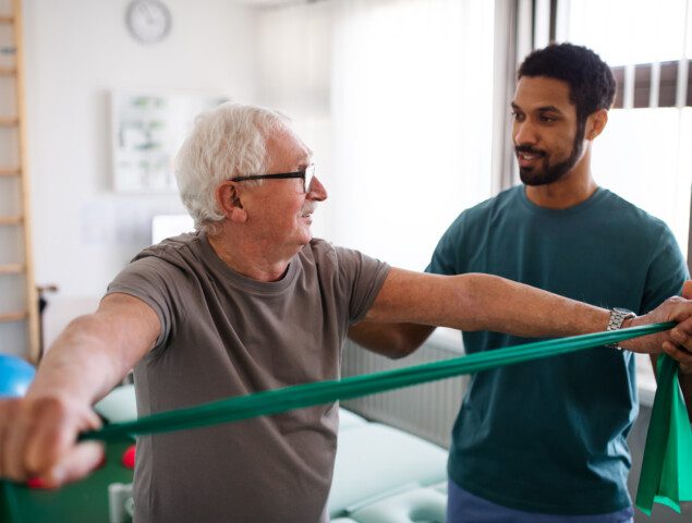 senior man practices physical therapy exercise with the help of his trainer