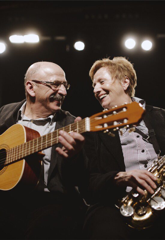 senior man plays acoustic guitar in a duet with a senior woman playing saxophone