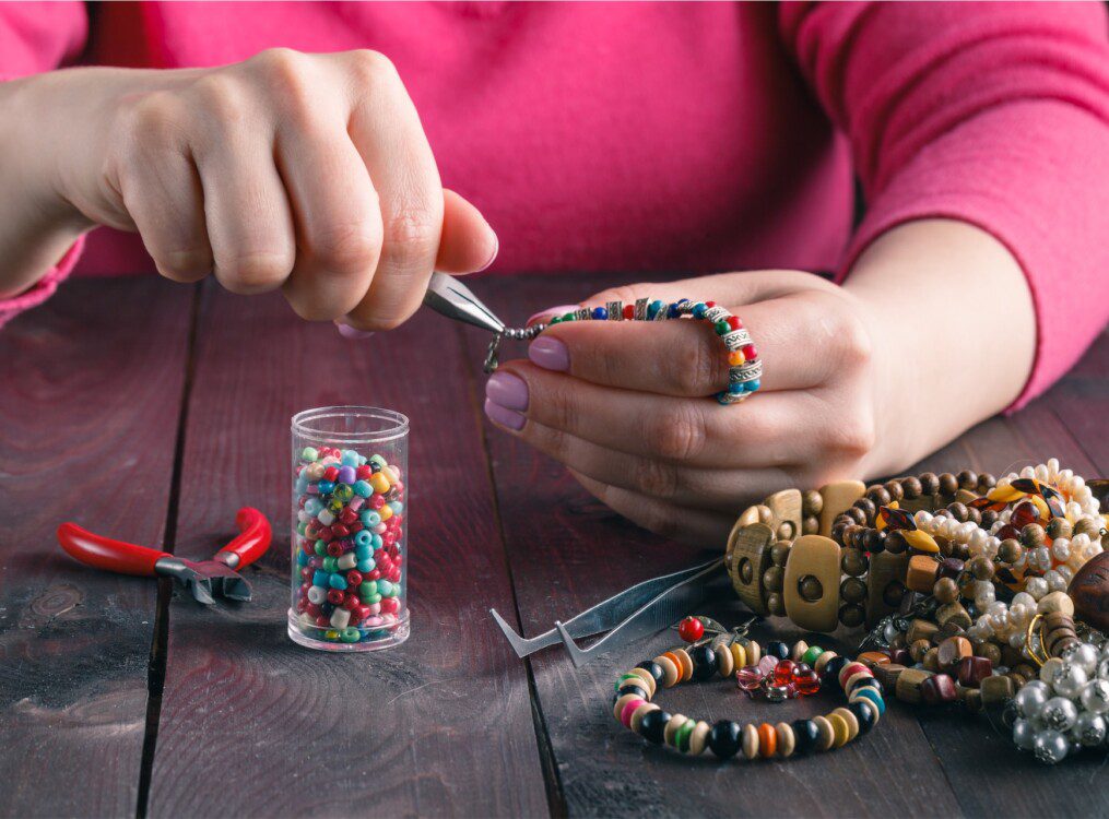 senior woman makes beaded bracelet at table