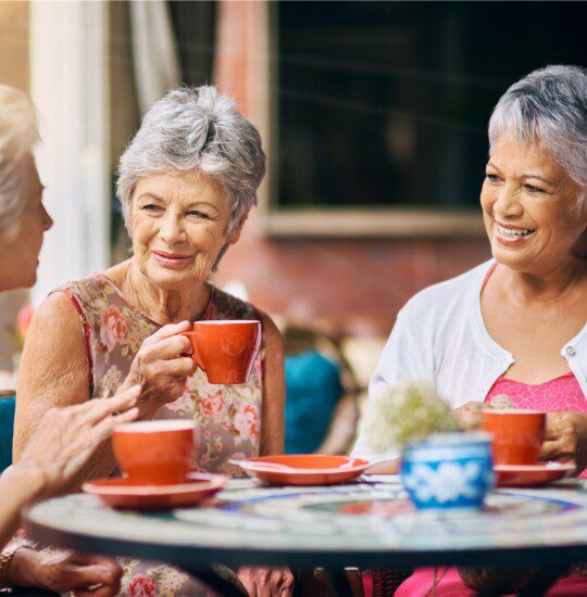 three senior women have a girls' brunch with coffee outside