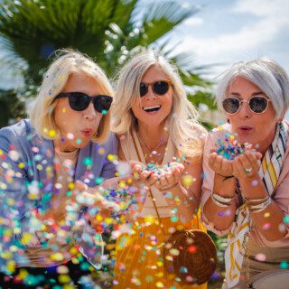 Fashionable senior friends having fun and celebrating by blowing colorful confetti in city street