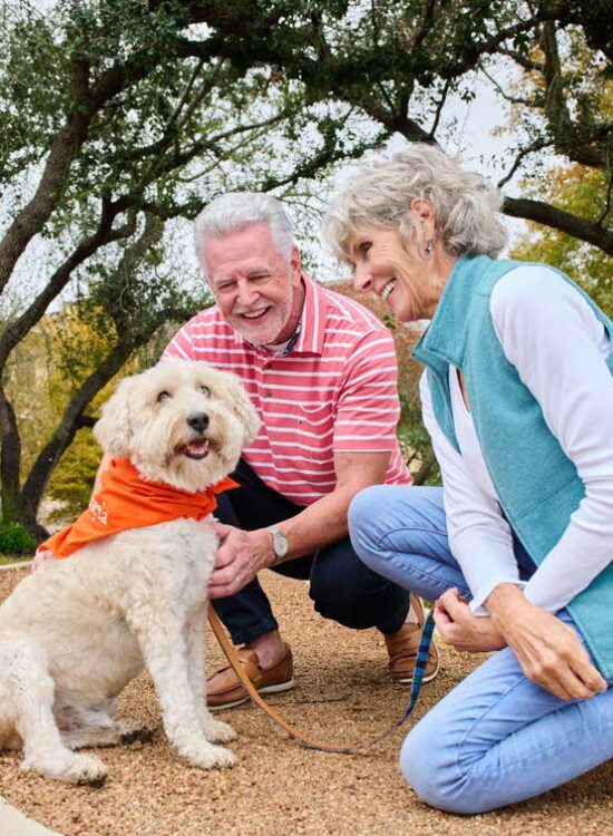 senior couple kneels to pet their dog on a scenic walking path at Oak Trace