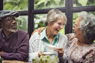 three senior friends laugh and enjoy tea together