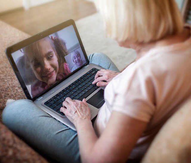 senior woman video chats with her smiling granddaughter on her laptop at home