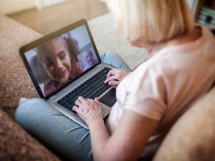 senior woman video chats with her smiling granddaughter on her laptop at home