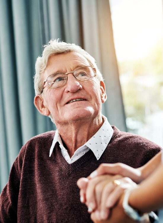senior man looks up at caregiver with gratitude while clasping her hand