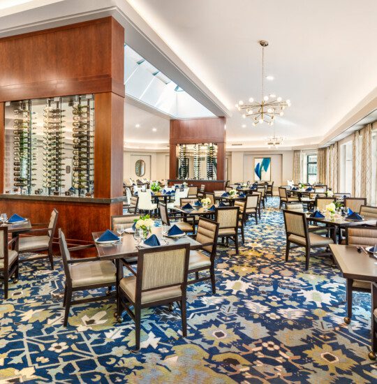 A modern dining room with patterned carpet and neatly set tables under chandeliers.