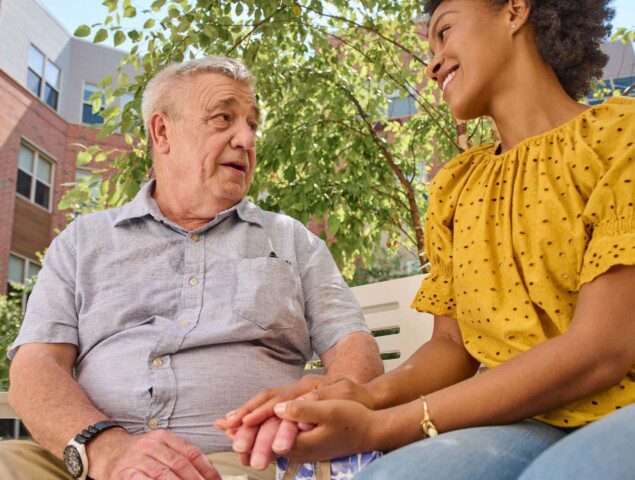 senior man chats with his adult daughter on a bench outside of Oak Trace Senior Living Community