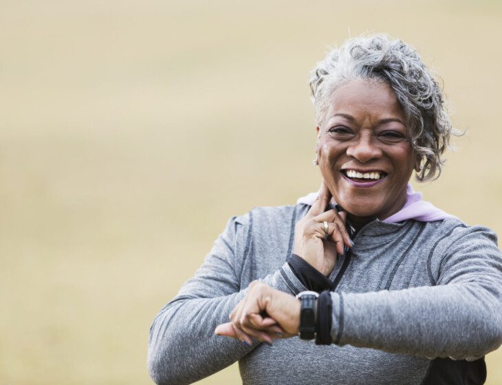 senior woman in athletic outfit smiles while checking her pulse after a walk