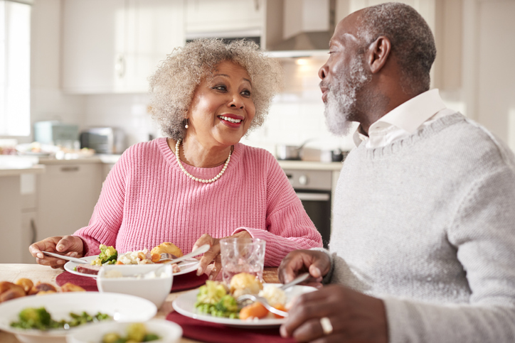 senior couple smile and enjoy a healthy dinner together in their apartment at Oak Trace Senior Living Community