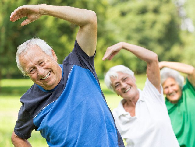 three seniors stretch and smile outdoors for a wellness class