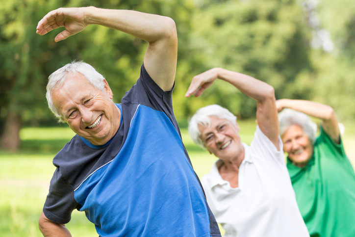 three seniors stretch and smile outdoors for a wellness class