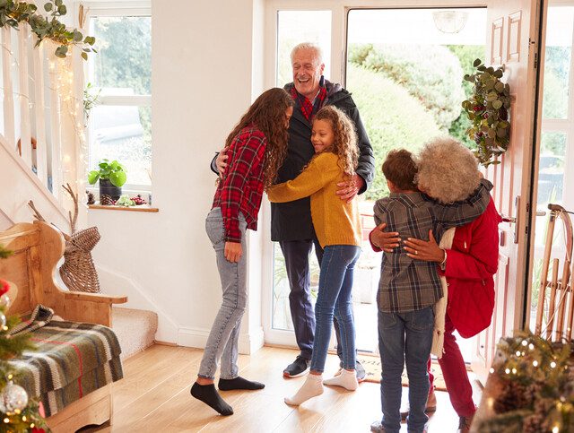 Excited Grandchildren Greeting Grandparents With Presents Visiting On Christmas Day.