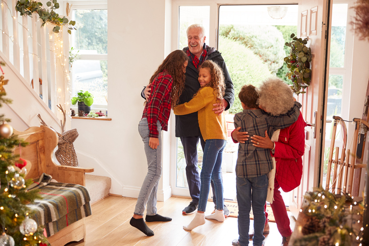 Excited Grandchildren Greeting Grandparents With Presents Visiting On Christmas Day.