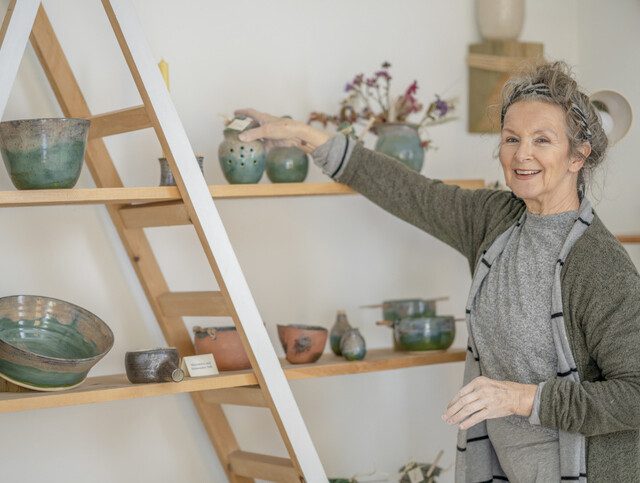 Senior woman smiles while placing pottery on a shelf