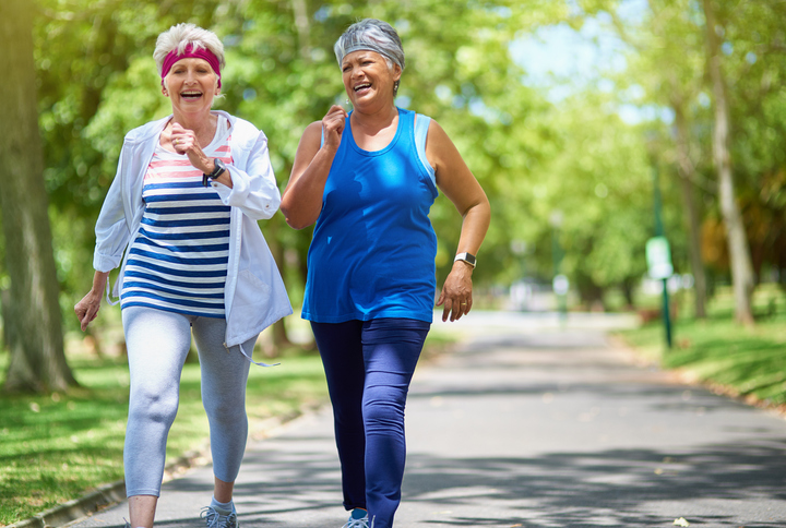 two senior women smile and talk while taking a brisk walk for exercise outside at Oak Trace Senior Living Community