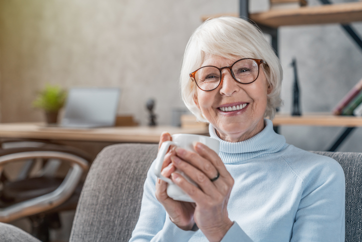 senior woman seated on cozy chair smiles and holds coffee mug