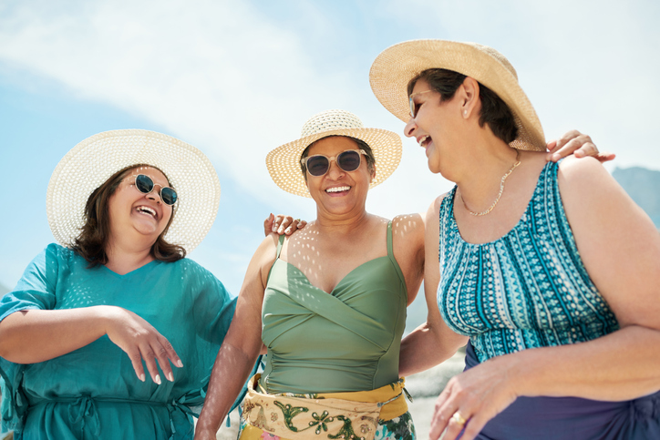 group of three senior women in bathing suits and stylish hats laugh together