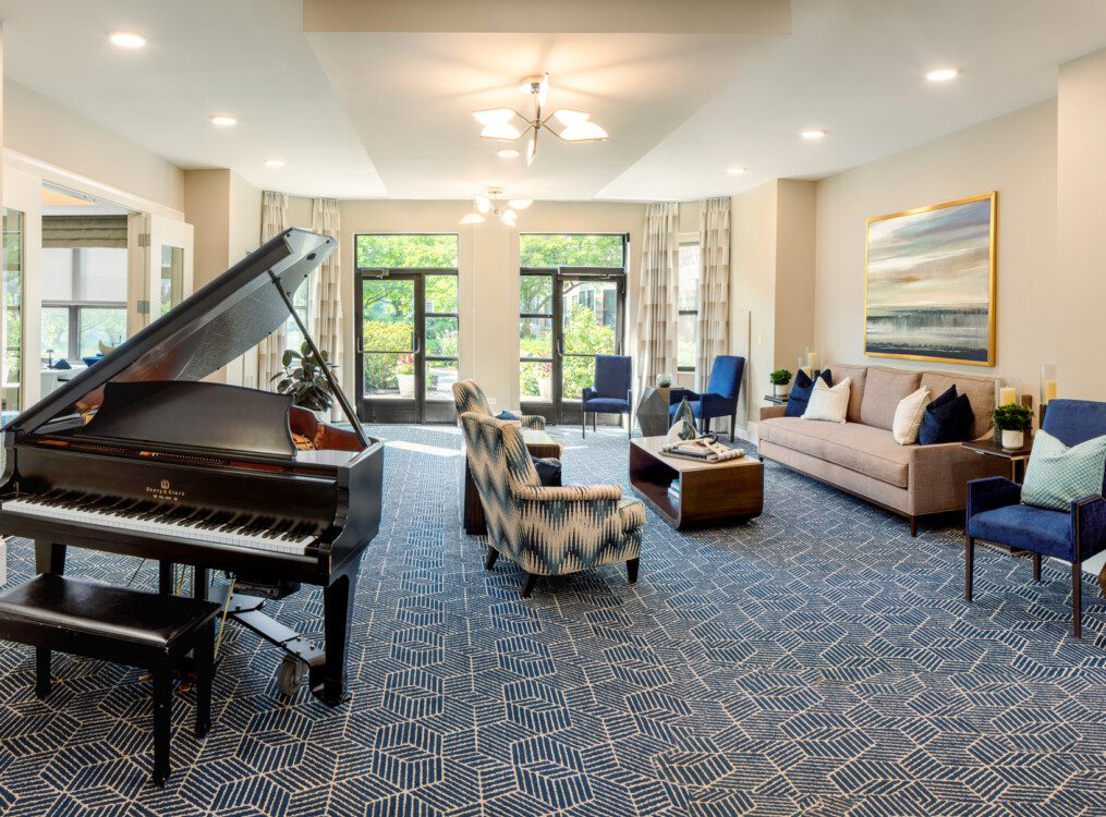 Elegant lounge and living room area with couch, chairs, and grand piano at Oak Trace Senior Living Community