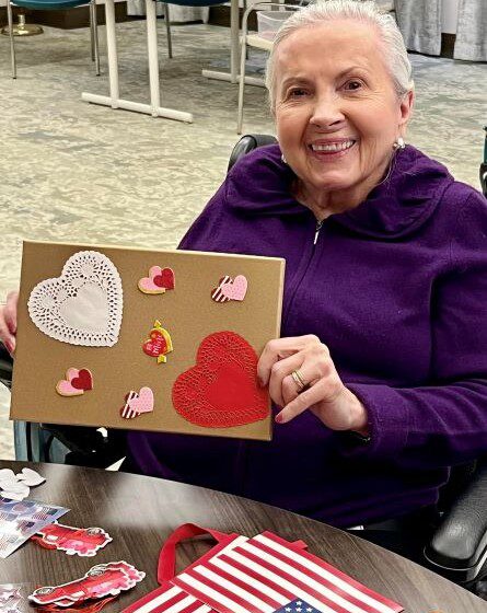 Oak Trace Senior Living resident smiles and holds up her valentine's day card creation
