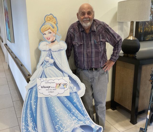 George Hlava, an Oak Trace Senior Living Community resident, smiles while posing next to a cut-out image of Cinderella