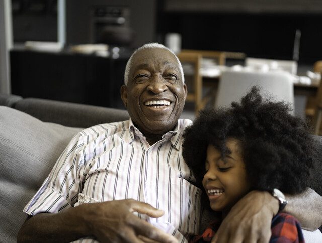 senior man sitting with his grandchild on the sofa smiling and laughing