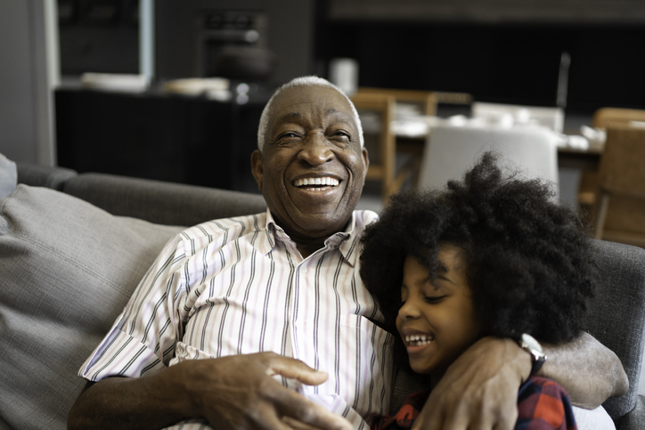 senior man sitting with his grandchild on the sofa smiling and laughing