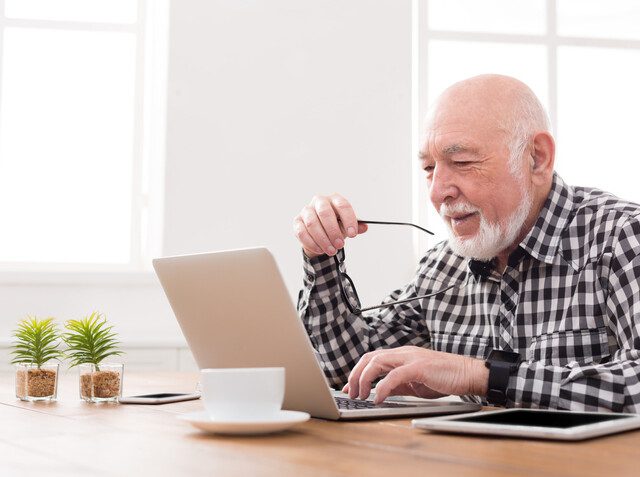 senior man smiles and browses the internet on his laptop