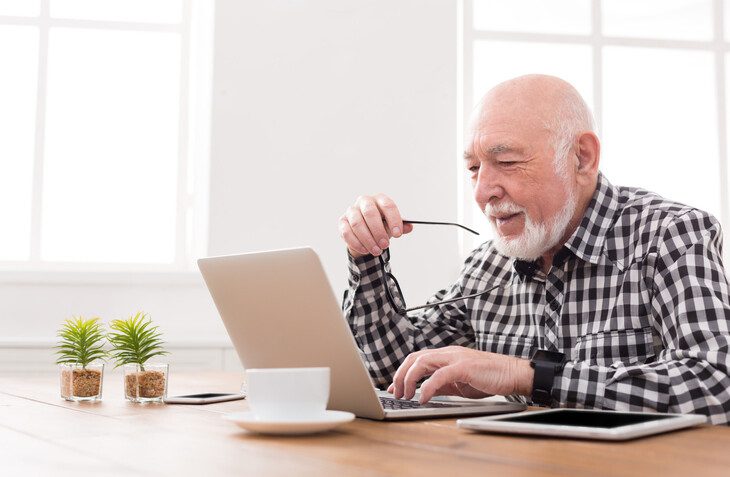 senior man smiles and browses the internet on his laptop