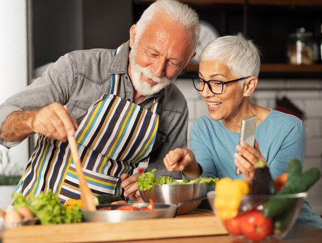Senior couple smiles and cooks new recipe together in the kitchen