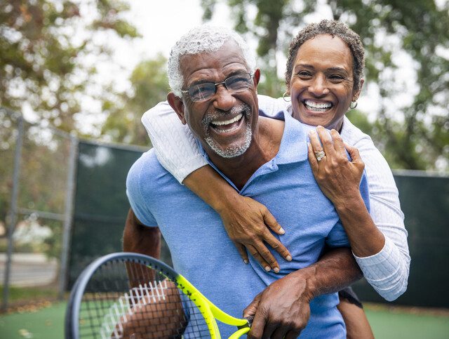 Senior man and woman smiling and embracing after a game of tennis outside