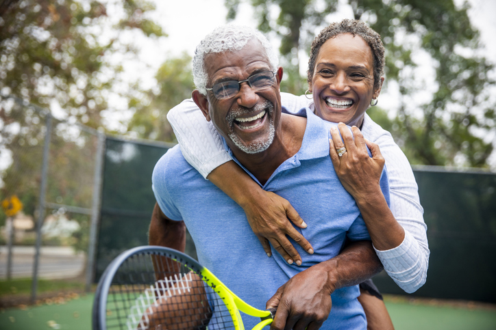 Senior man and woman smiling and embracing after a game of tennis outside