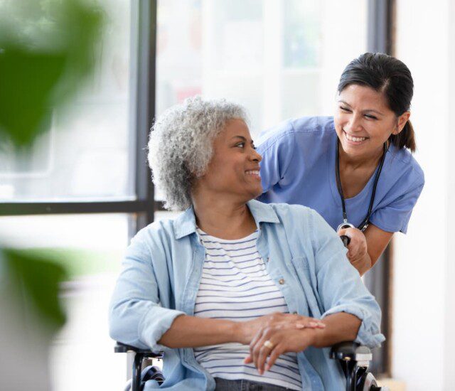 Senior woman in wheelchair looks over her shoulder and smiles at her caretaker