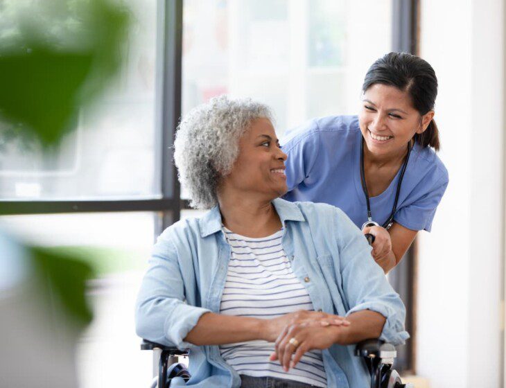 Senior woman in wheelchair looks over her shoulder and smiles at her caretaker