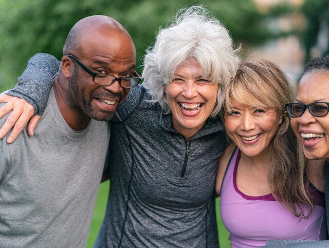 group of four seniors in athletic clothing smile and wrap their arms together
