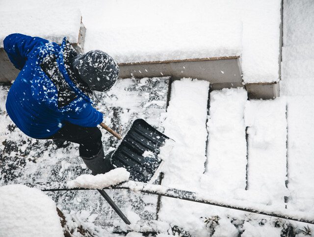 Older adult man shoveling snow on the stairwell outside his home