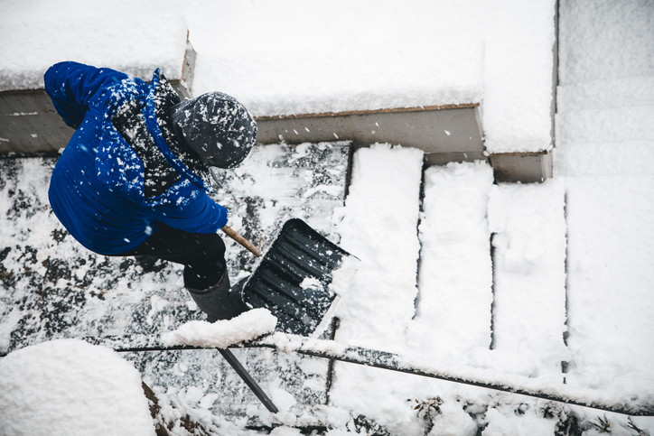 Older adult man shoveling snow on the stairwell outside his home