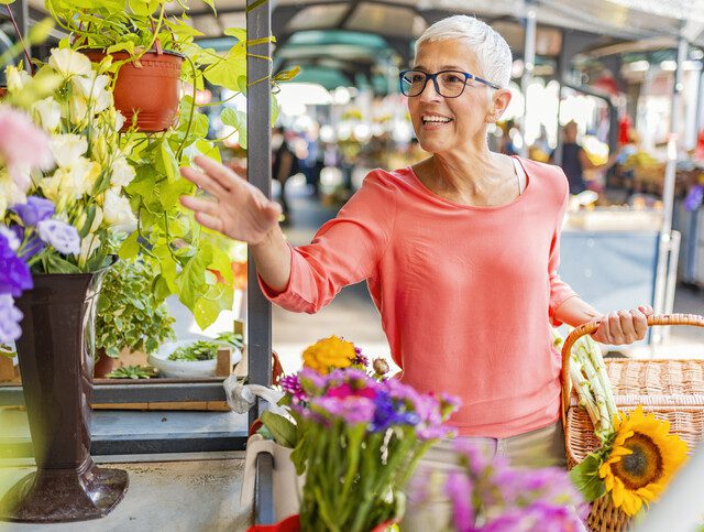 Senior woman smiles and reaches for fresh flowers at a farmers market in Downer's Grove, Illinois