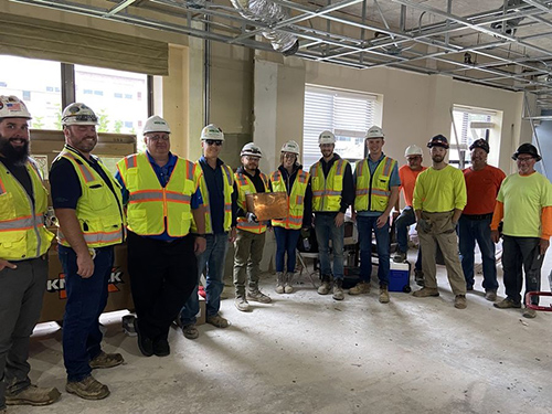 Group of construction workers in yellow vests smile, posing with the time capsule found at senior living community