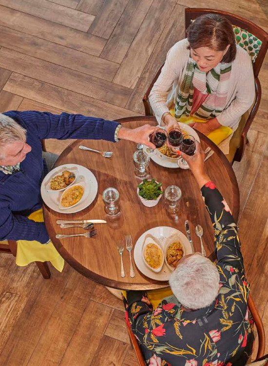 three seniors toast wine glasses together over lunch at Oak Trace Senior Living Community