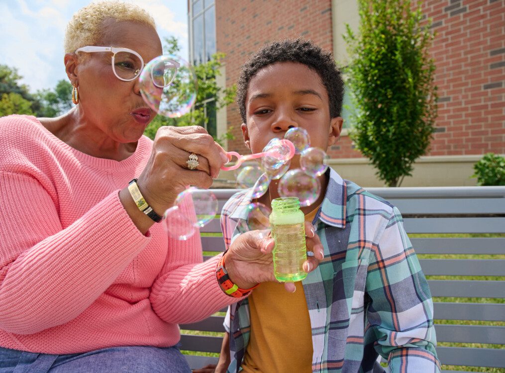 grandmother helps her grandson blow bubbles outside of her senior living community