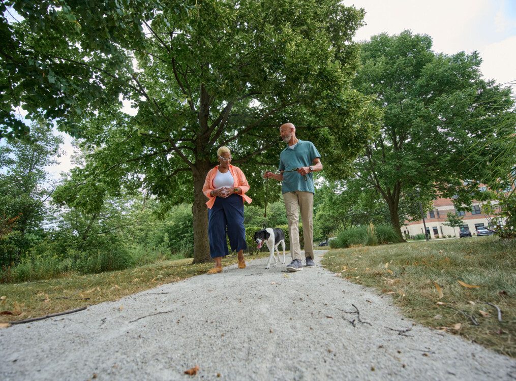 senior man and woman talk and walk their dog outside of their senior living community
