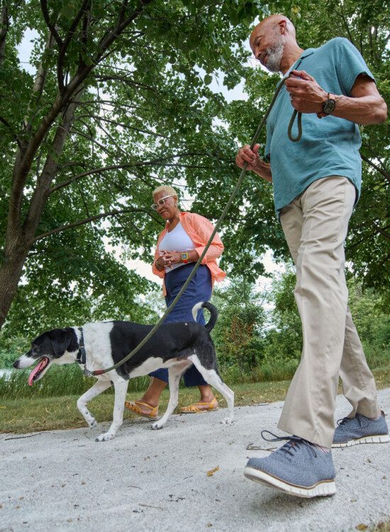 senior man and woman walk their dog on a scenic landscaped path outside of their senior living community